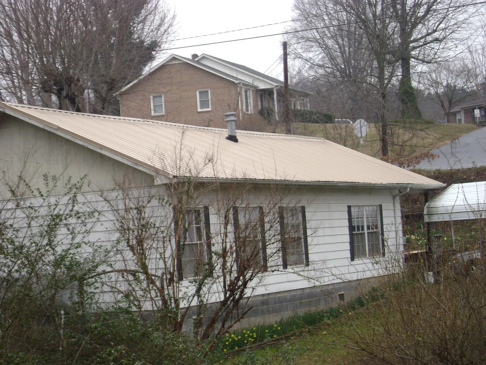 Tan metal roof on a white sided house set into a hillside — Commercial Roofing by Roofing Brothers in Frankfort